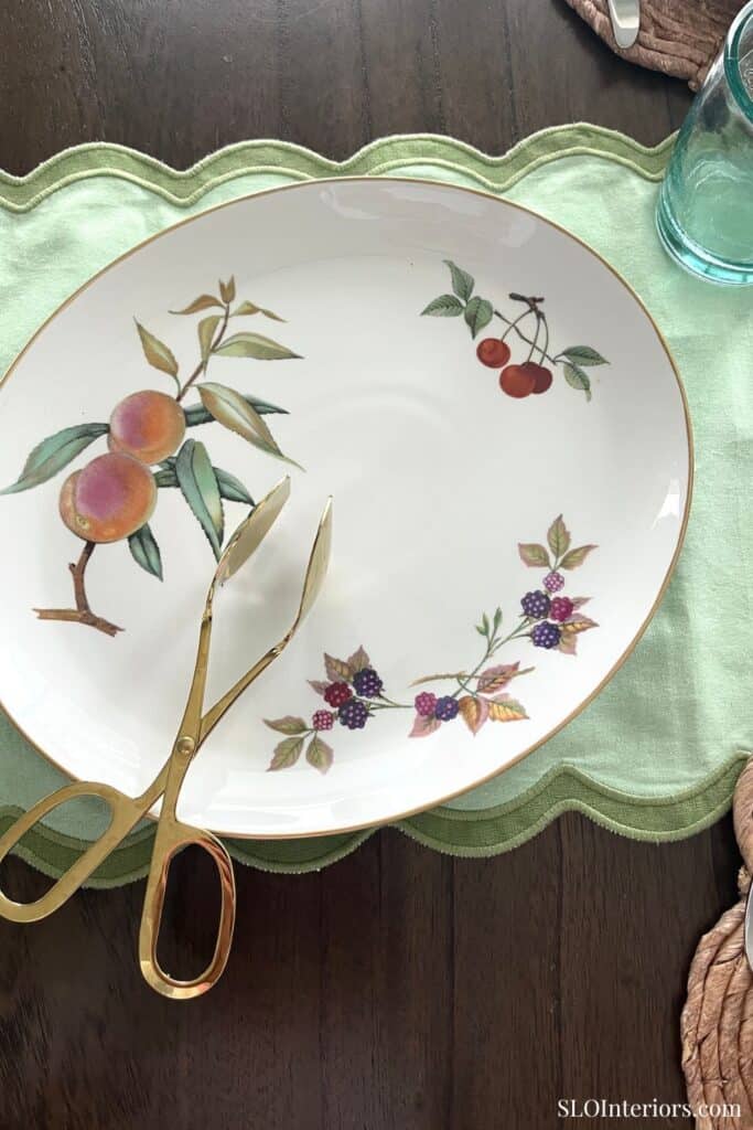 Decorative ceramic plate with fruit and berry design on a green tablecloth.