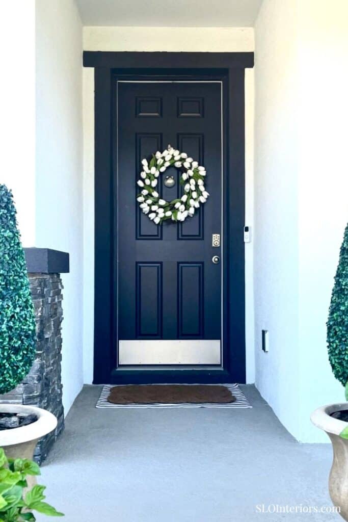 Front door with a white floral wreath and black frame, welcoming entryway.