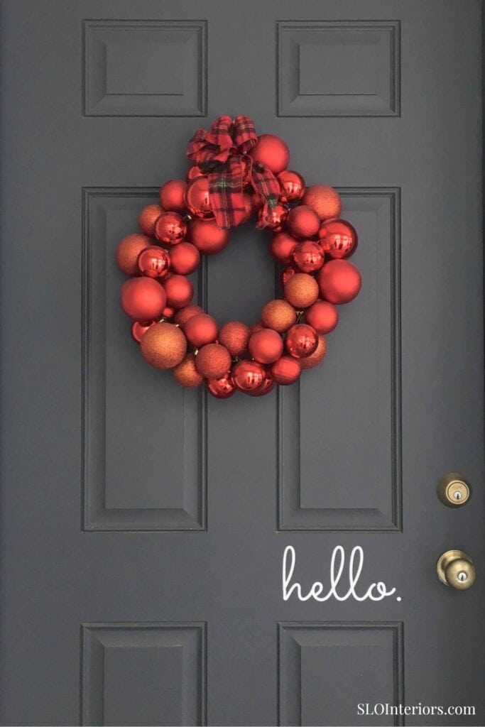 Festive red Christmas wreath hanging on a dark gray door with 'hello' text.