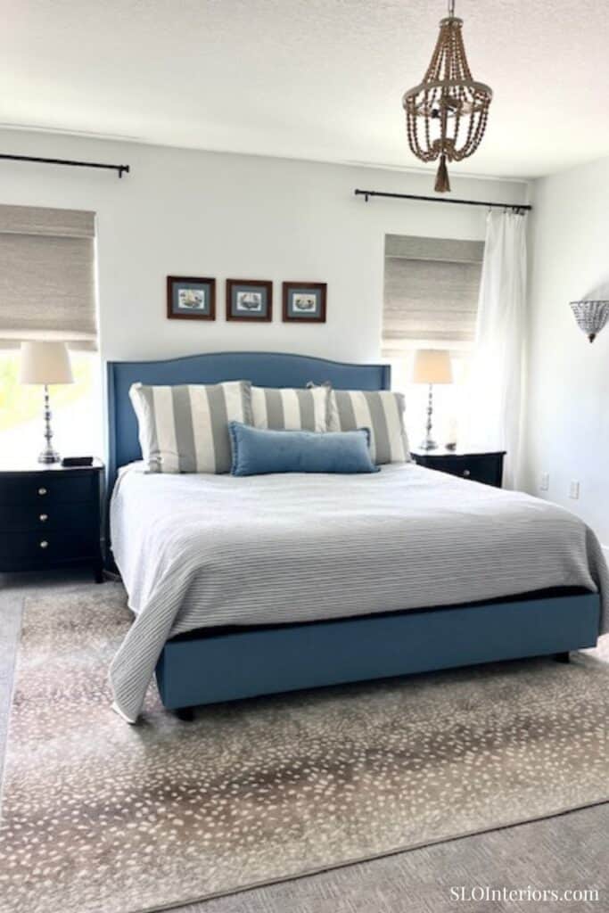 A cozy bedroom with a blue upholstered bed, striped pillows, and modern decor.