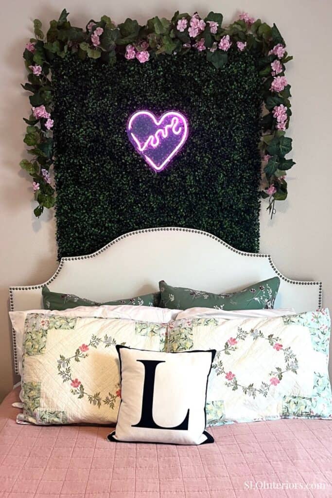 Decorative bedroom with floral wall, neon love sign, and cozy pillows.