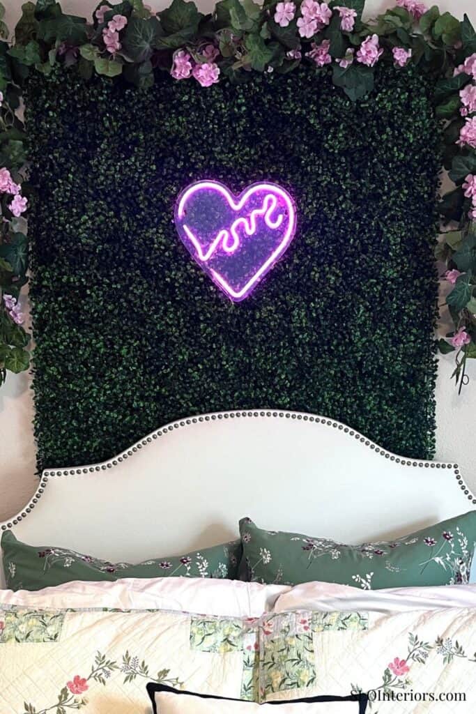 Decorative wall with neon heart and 'love' sign above bed with floral pillows.
