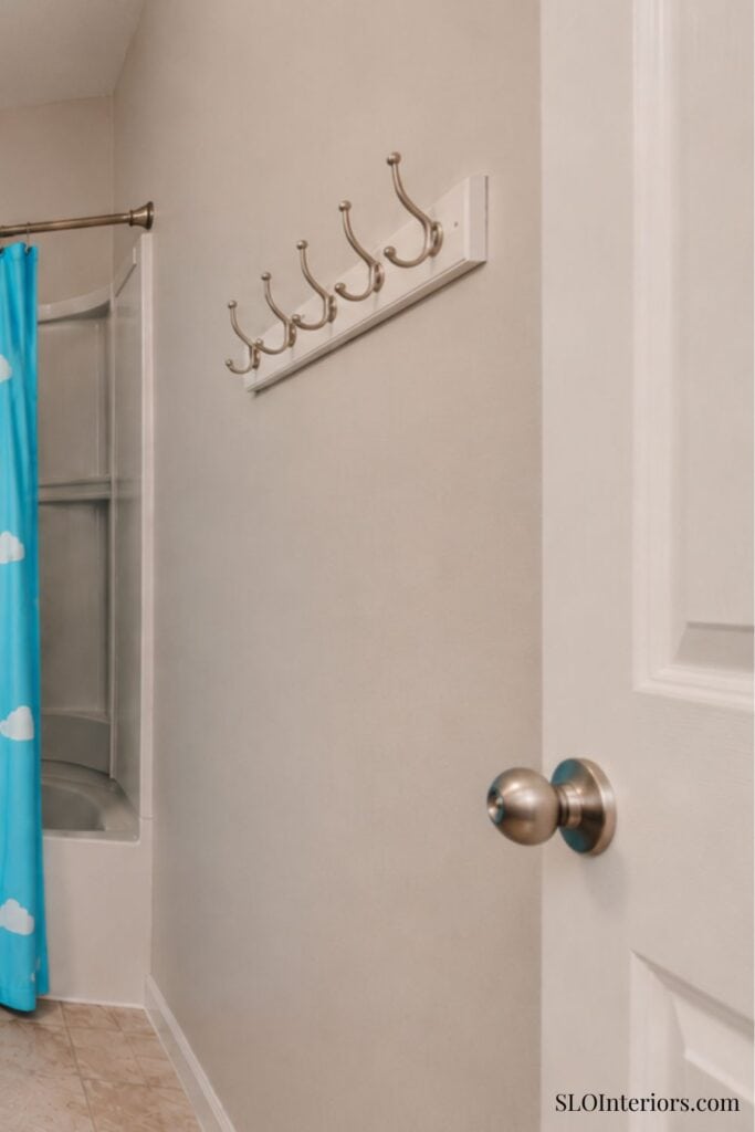 White wall with coat hooks near bathroom with shower curtain and door handle.