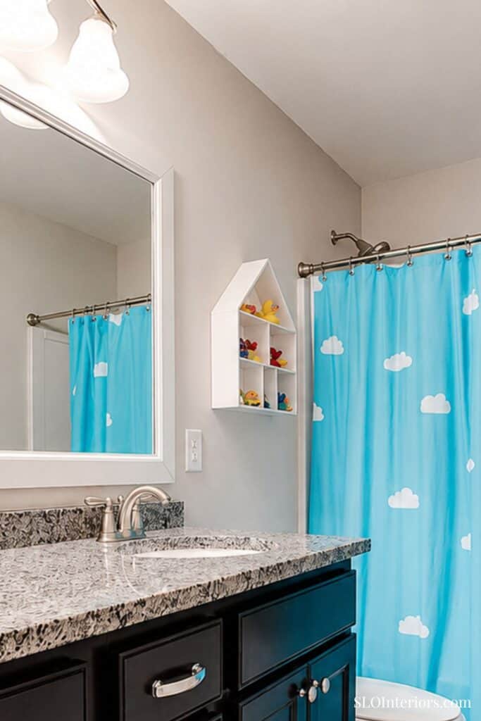 Modern bathroom with granite countertop, white shelves, and blue cloud shower curtain.