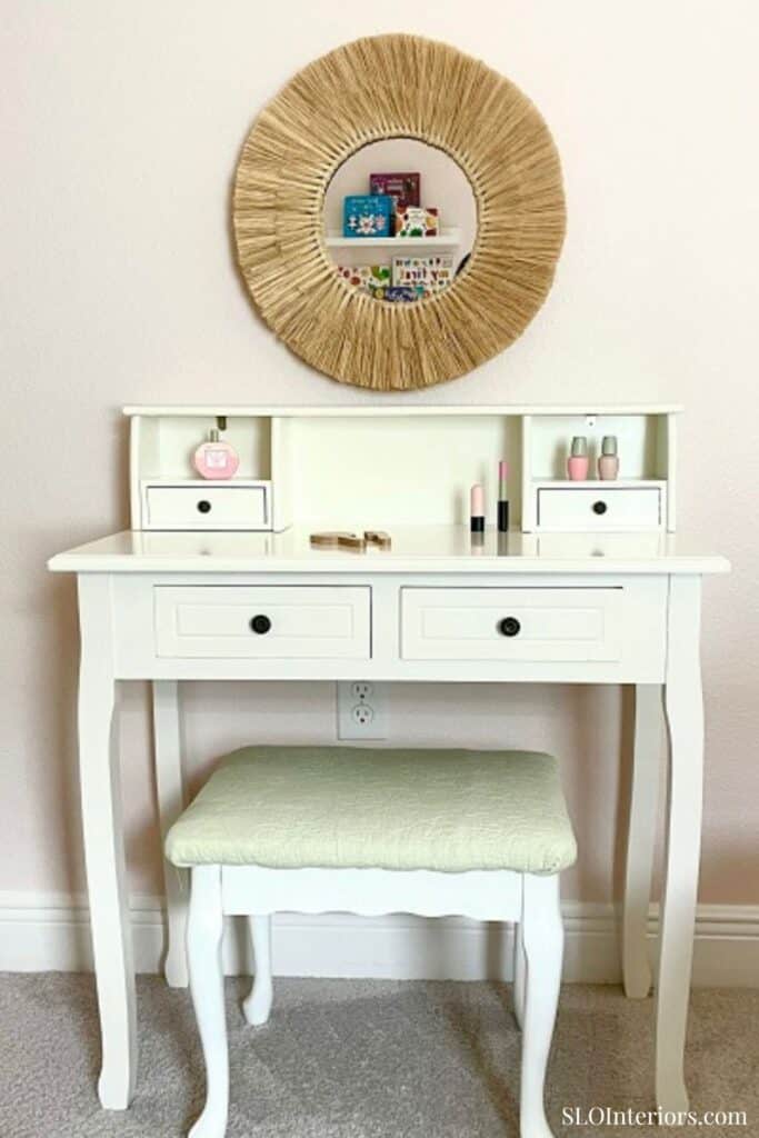 White vanity table with a matching stool and decorative mirror in a bright room.