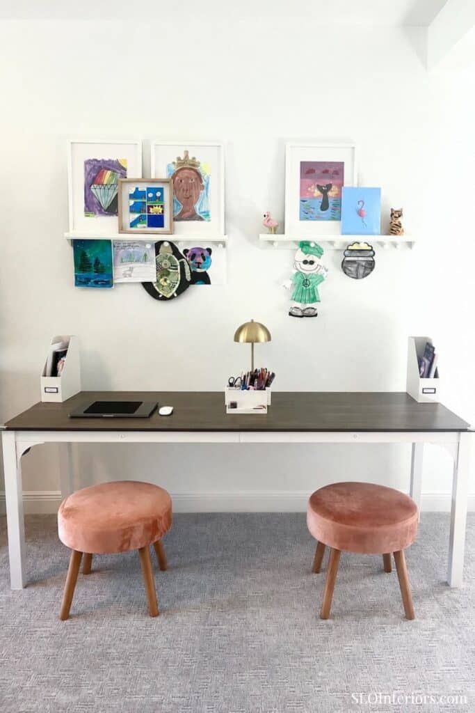 Modern home office with artwork and two pink stools at a desk.