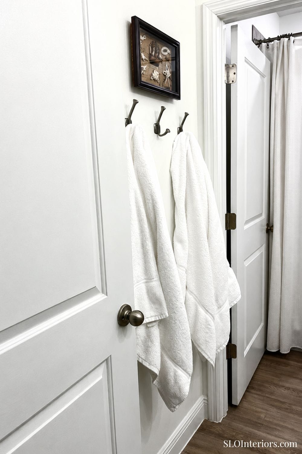 White towels hanging on hooks in a modern bathroom with white walls and door.