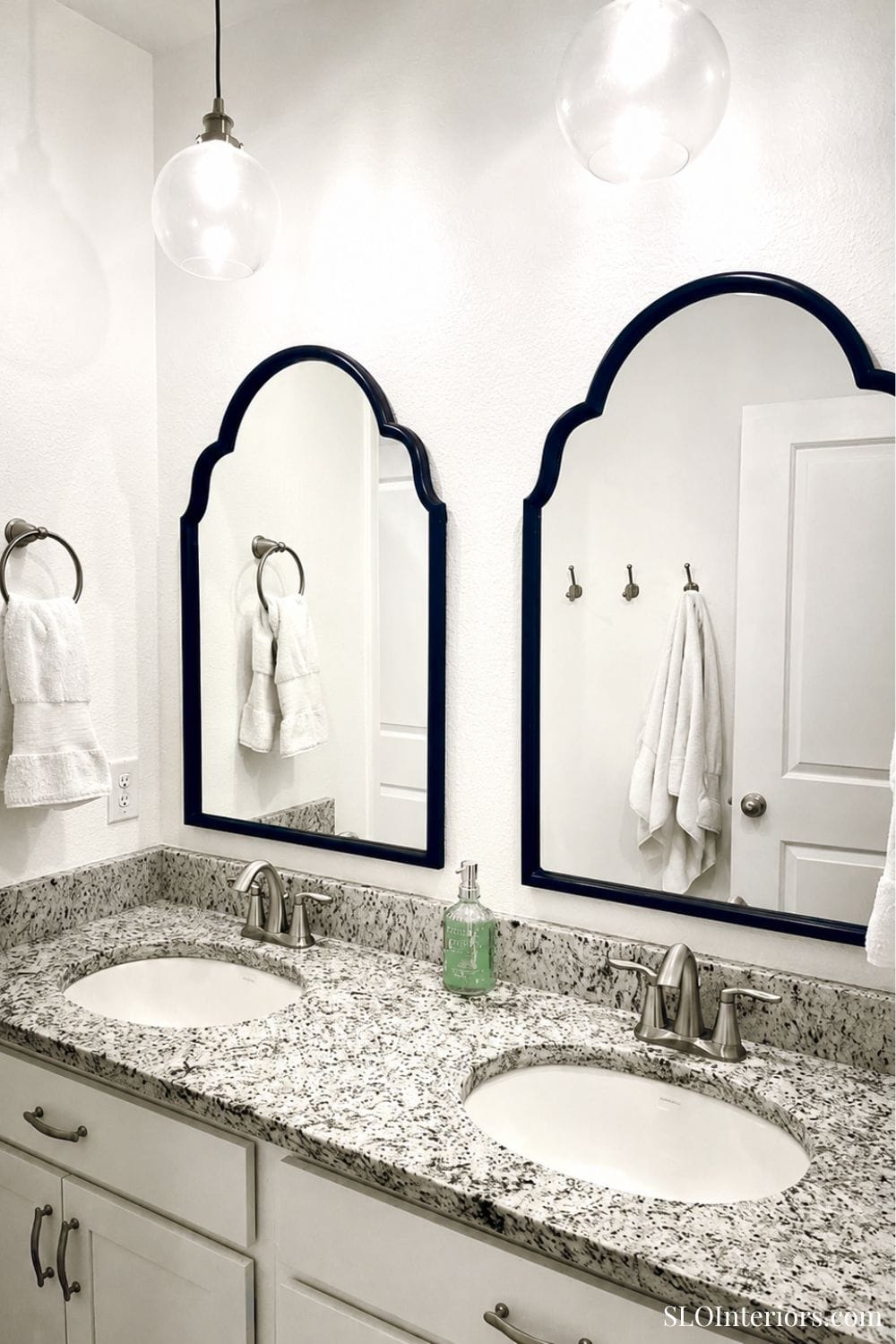 Modern bathroom with dual sinks, granite countertop, and decorative mirrors.