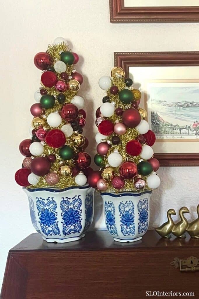 Festive Christmas trees decorated with red, white, green, and gold ornaments in blue and white pots.