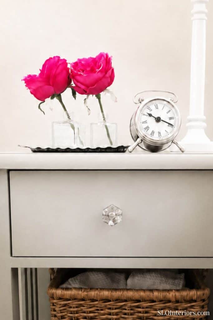 Pink peonies in glass vases with clock on white bedside table.