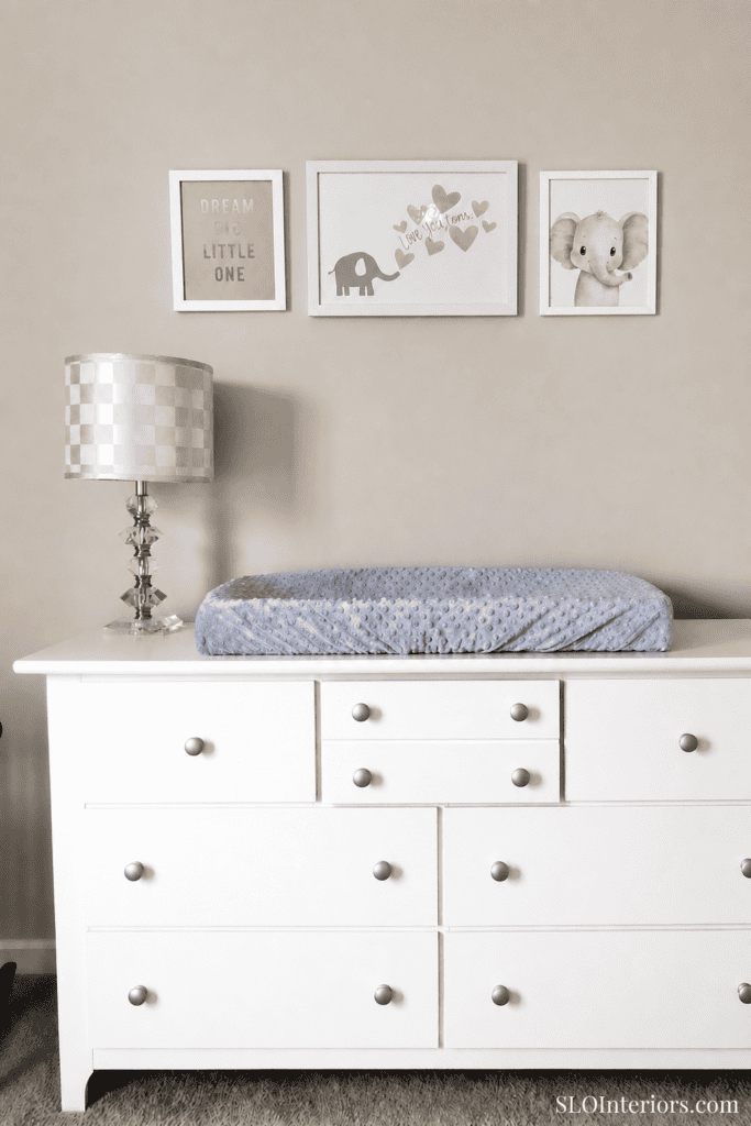 Modern baby changing station with white dresser and wall art in nursery.