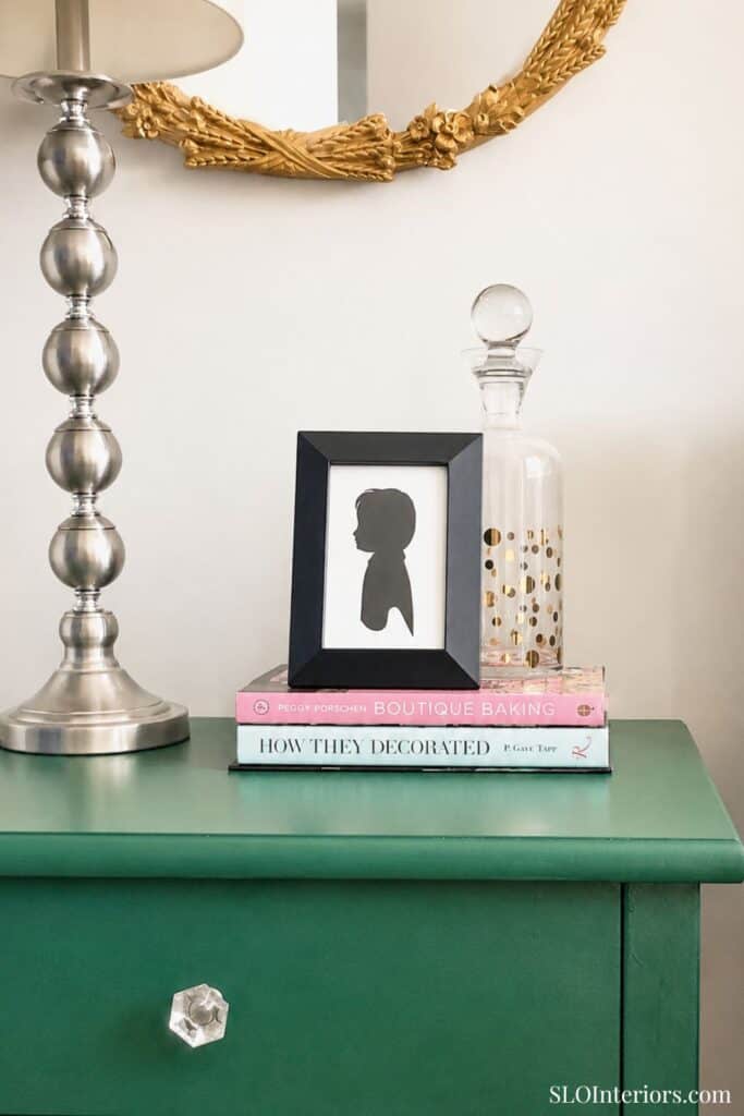 Decorative side table with lamp, framed silhouette, and glass jar in modern interior.