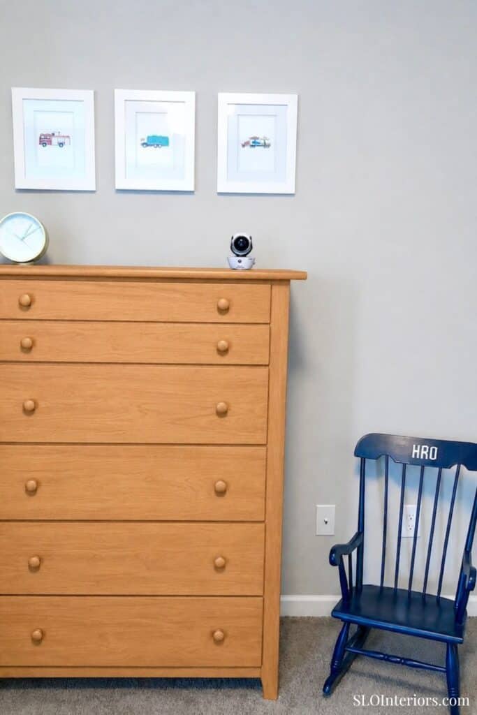 Modern bedroom with wooden dresser, blue rocking chair, and framed art.