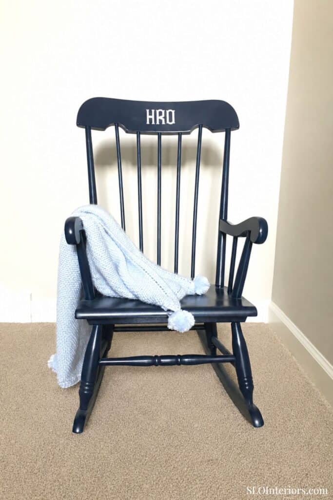 Black wooden rocking chair with a light blue blanket draped over it, on beige carpet.