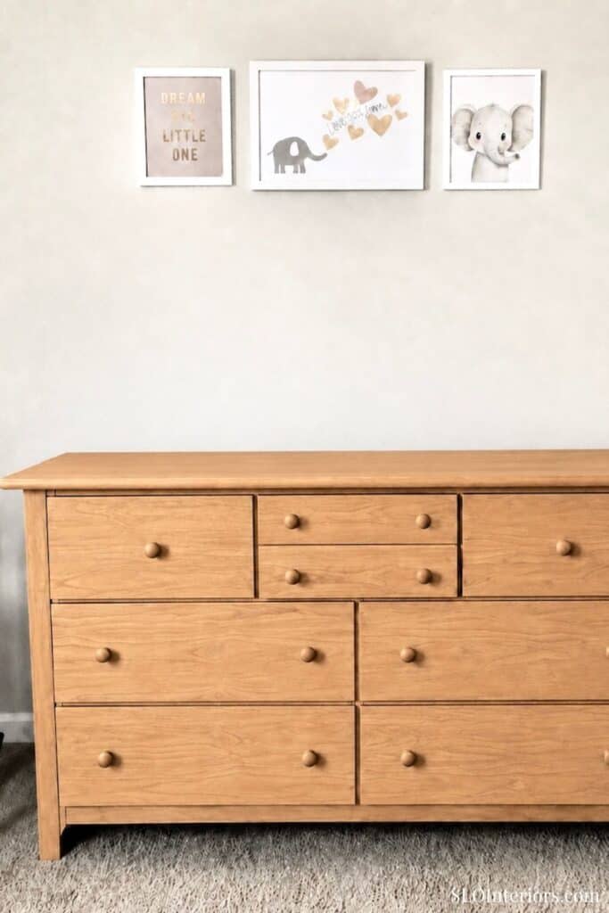 Wooden dresser with nine drawers in a modern nursery with wall art.