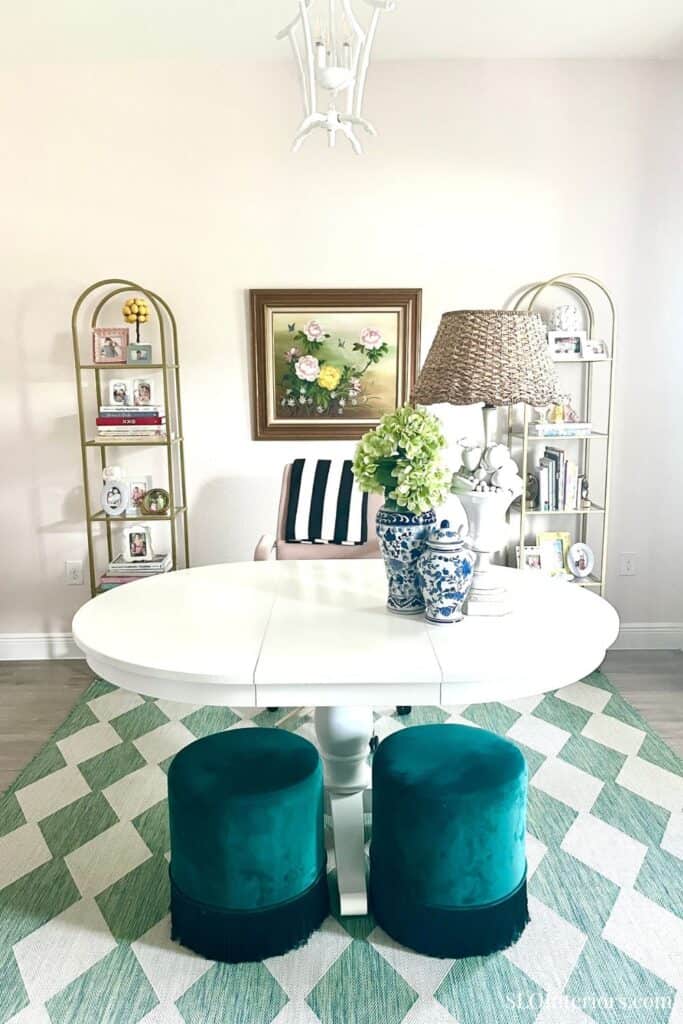 Elegant living room with white oval table, teal velvet stools, and decorative shelves.
