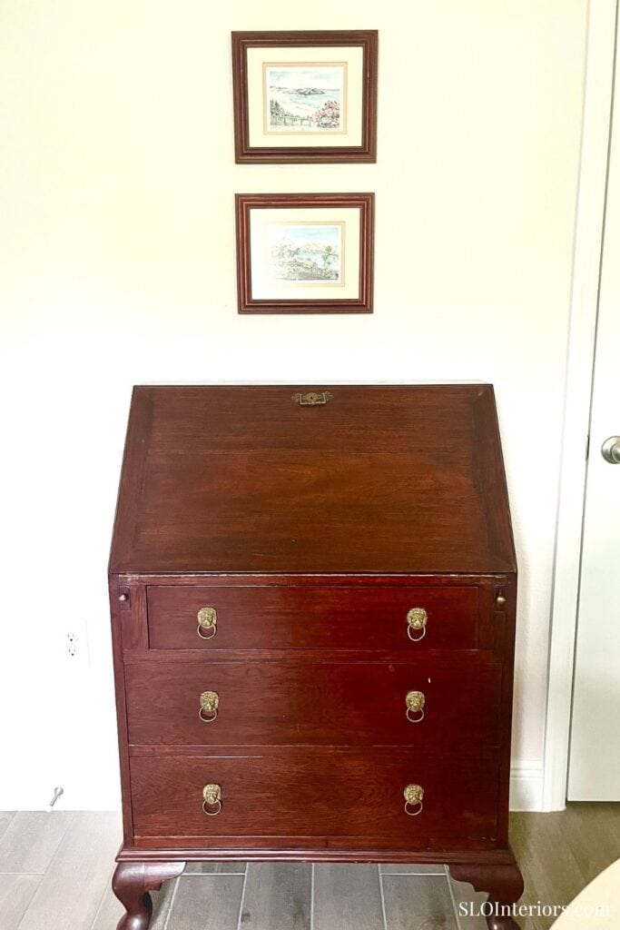 Elegant wooden secretary desk with three drawers and brass handles in a modern room.