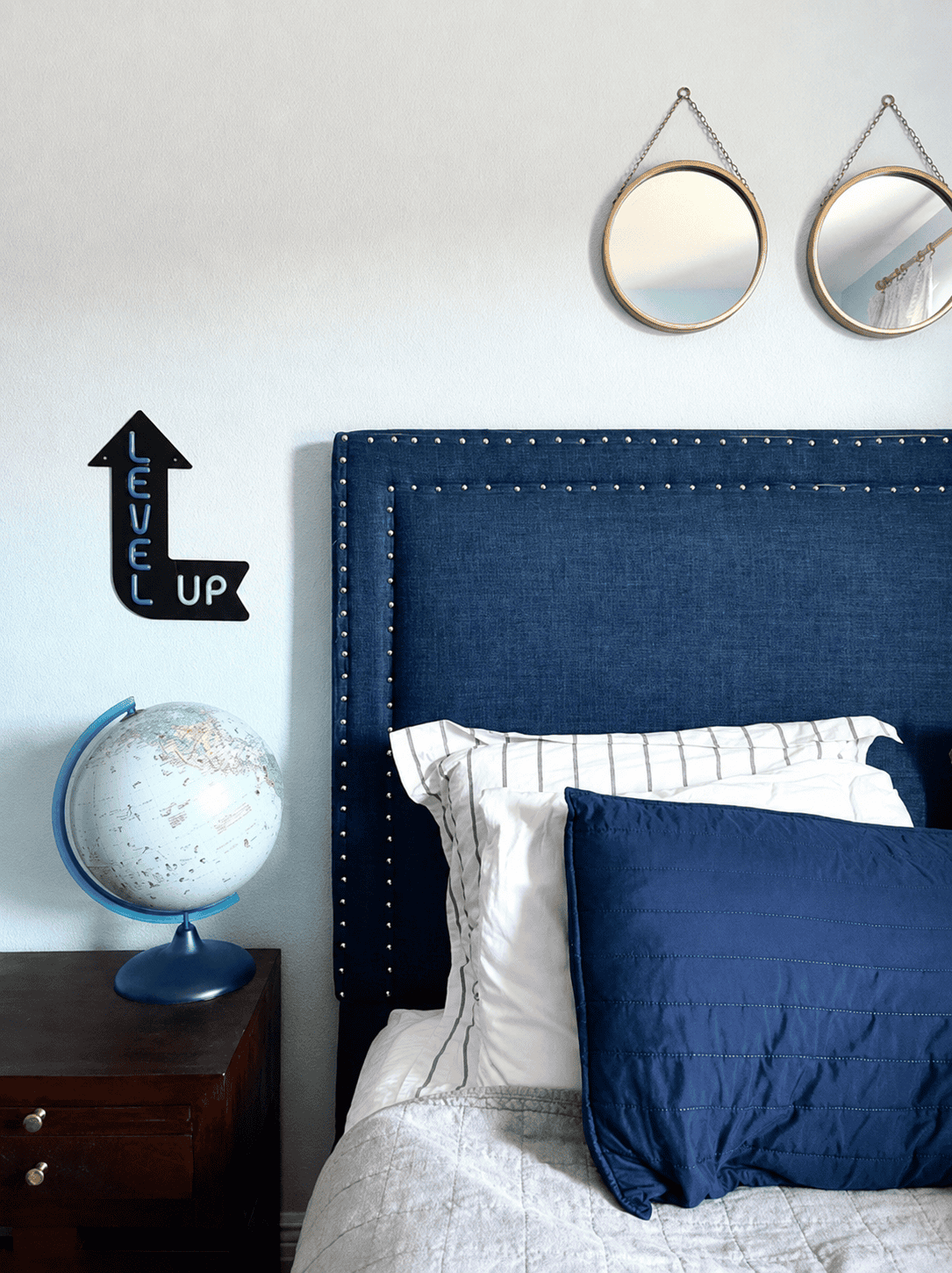 Modern bedroom with navy upholstered headboard, globe, and decorative mirrors.