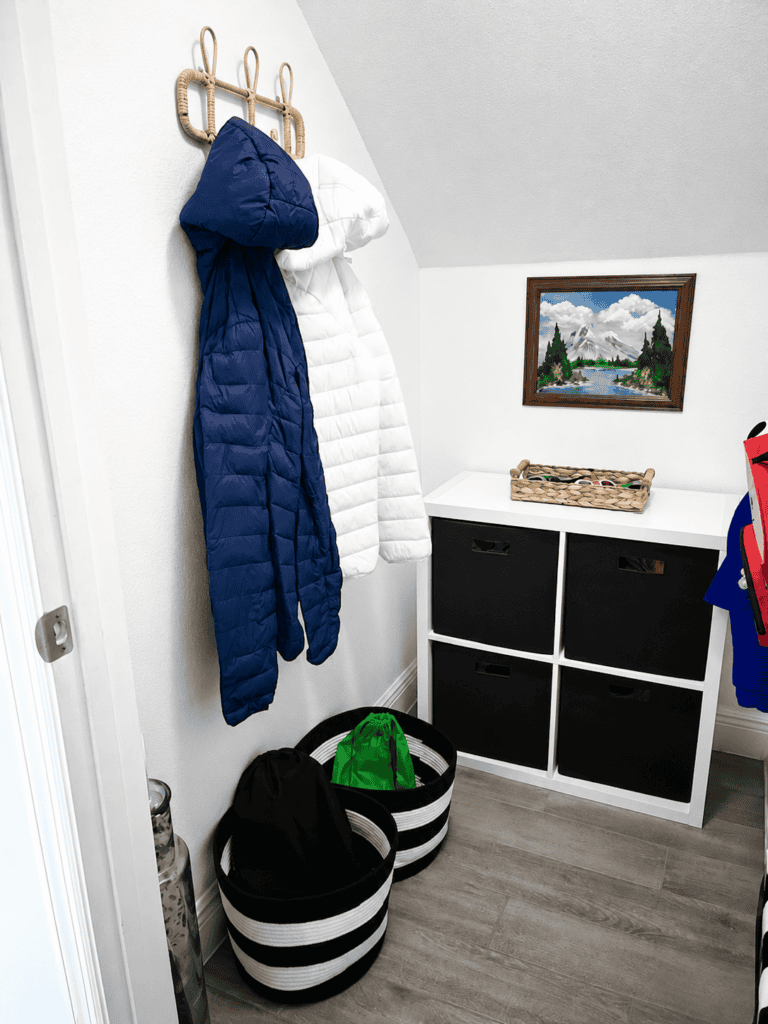 Coat hooks with blue and white jackets in a modern entryway with storage baskets.