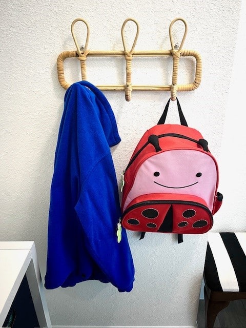 Colorful children's backpack and blue jacket hanging on wall hooks in a modern home.
