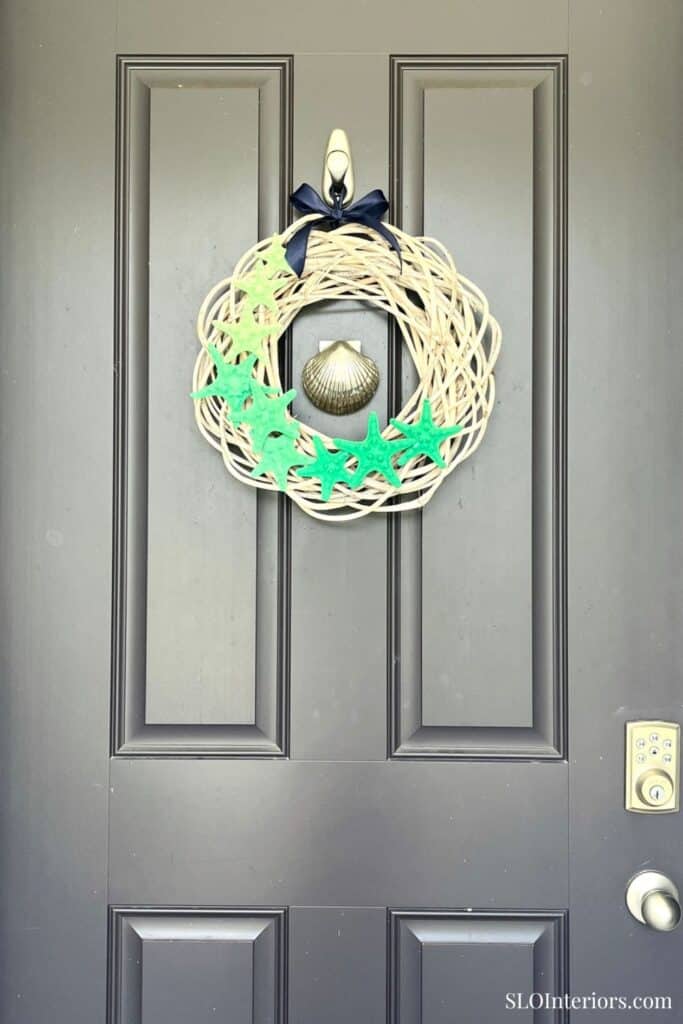 Decorative holiday wreath with starfish and seashell on gray door.