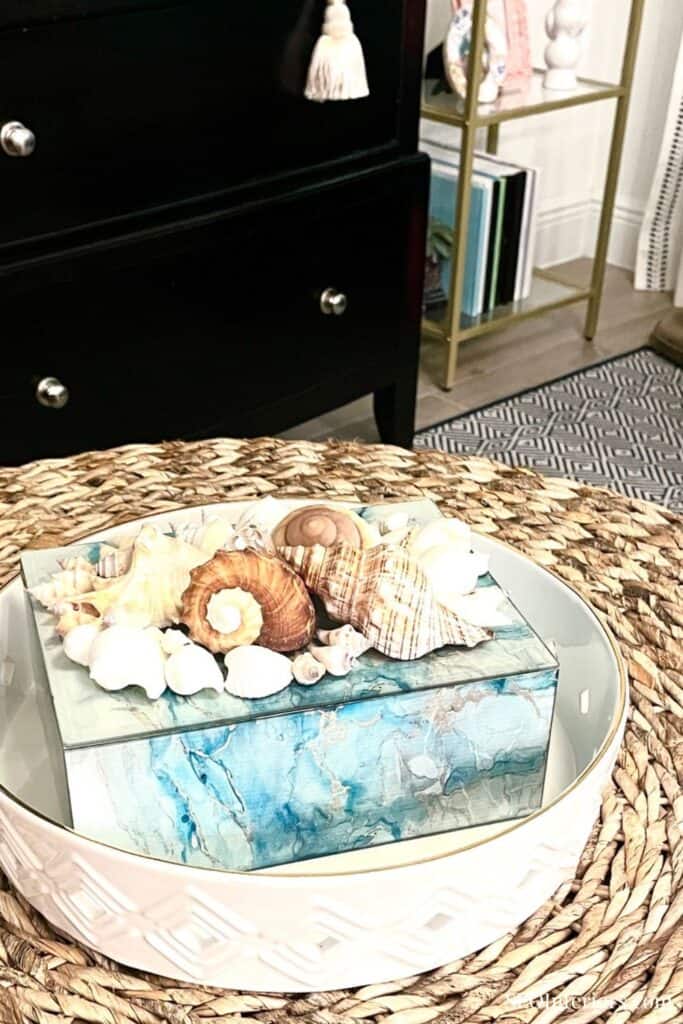 Decorative seashells and a blue marble box on a glass tray in a stylish interior setting.