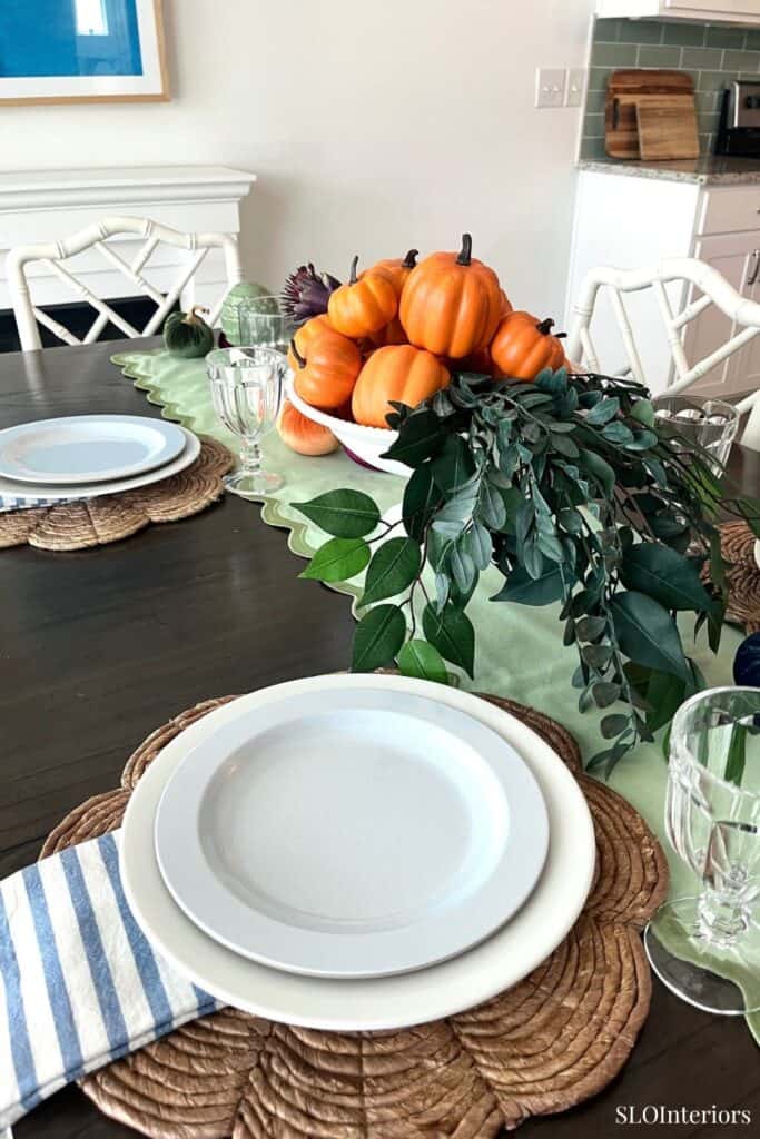Fall-themed dining table with pumpkins and greenery centerpiece in modern kitchen setting.