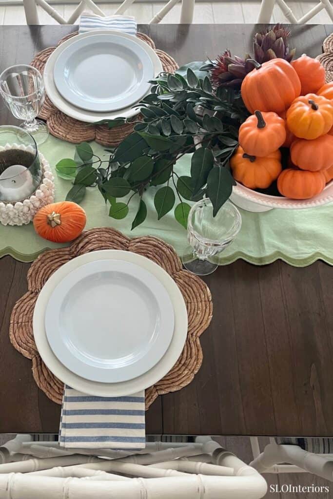 Fall-themed dining table setup with pumpkins, greenery, and seasonal decor.