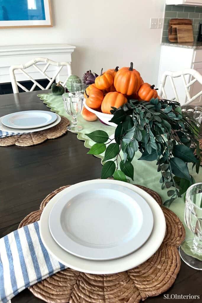 Fall-themed dining table with pumpkins and greenery centerpiece in a modern kitchen.
