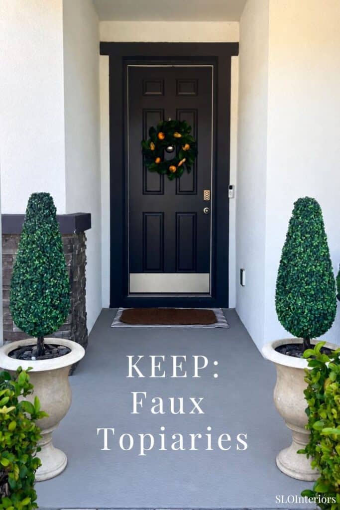 Front door with festive wreath and decorative topiary plants on porch.