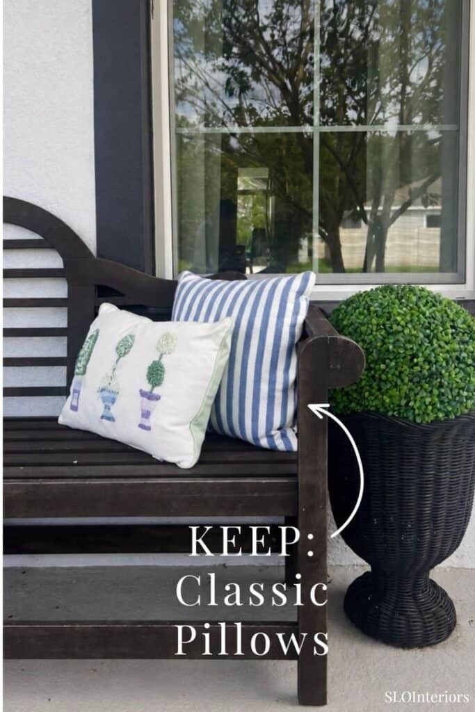 Outdoor wooden bench with striped and embroidered pillows near a window and potted plant.