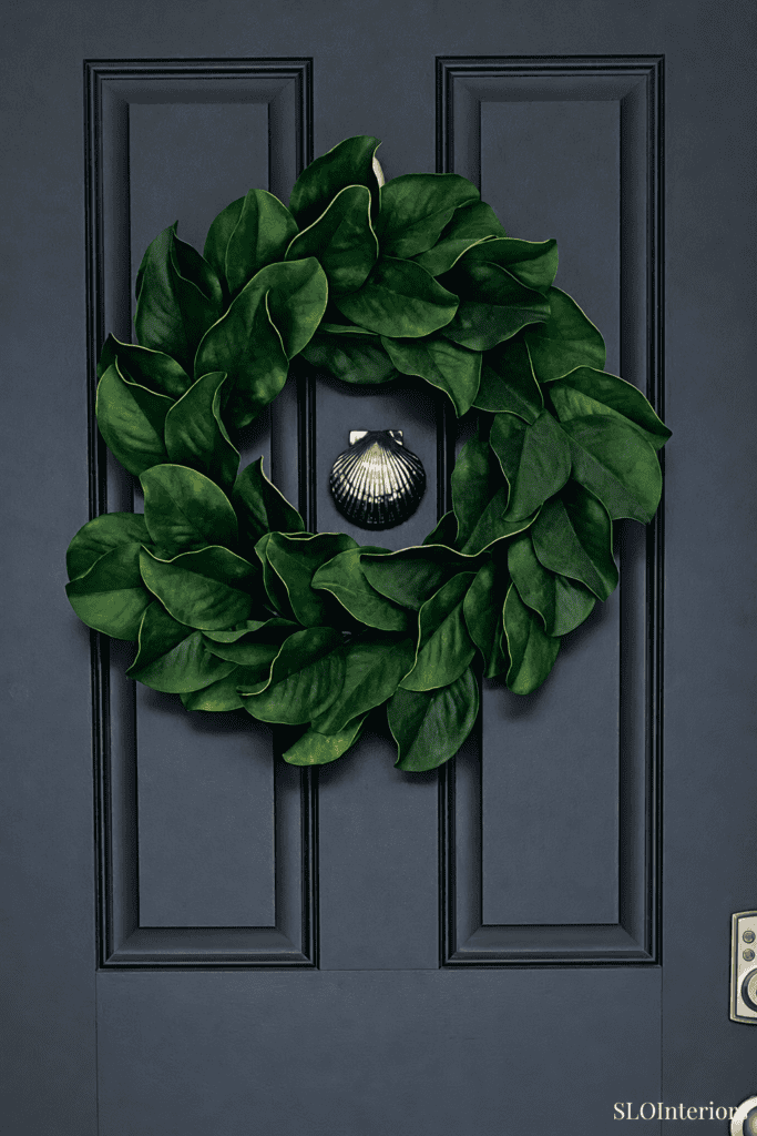 Elegant green leaf wreath hanging on a dark blue door with a small decorative ornament.