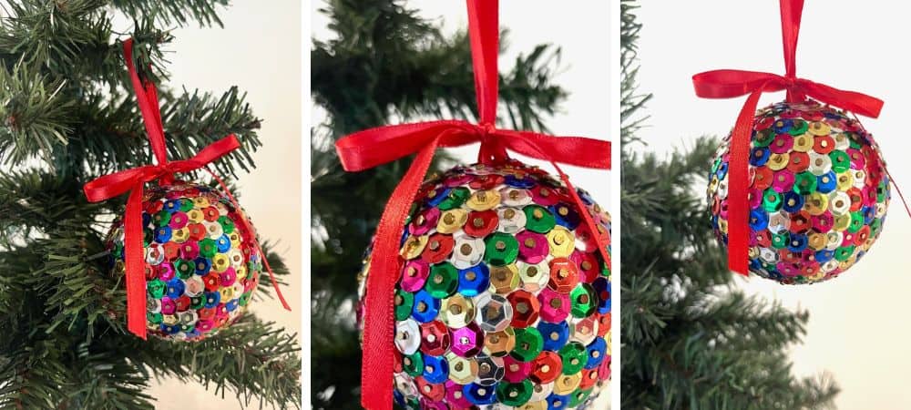 A colorful sequin Christmas ornament hanging on a tree with a red ribbon.