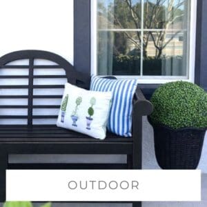 Outdoor black bench with decorative pillows and potted plant by window.
