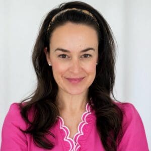 Smiling woman in pink blouse with dark hair and headband, indoor setting.